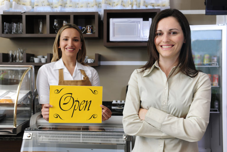 two ladies in business holding an open sign